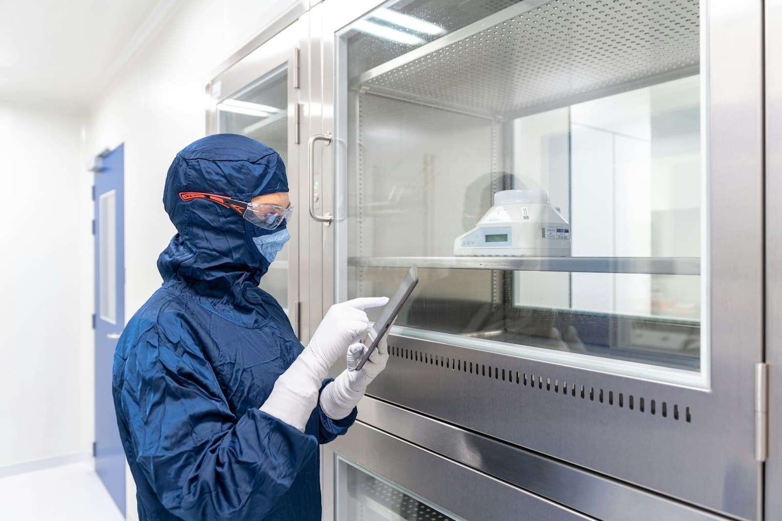 A quality specialist in cleanroom gear reviewing records on a tablet